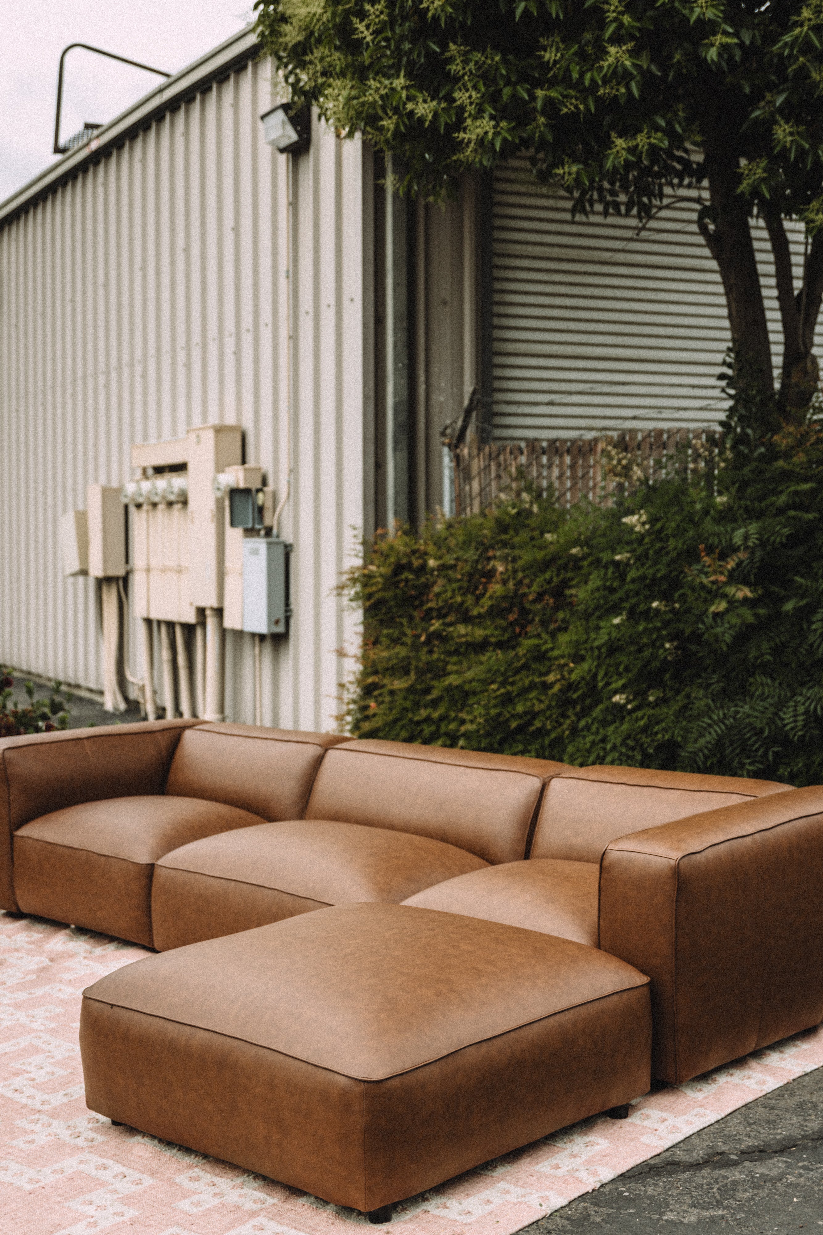 Brown sectional sofa on a patio with a building and trees in the background
